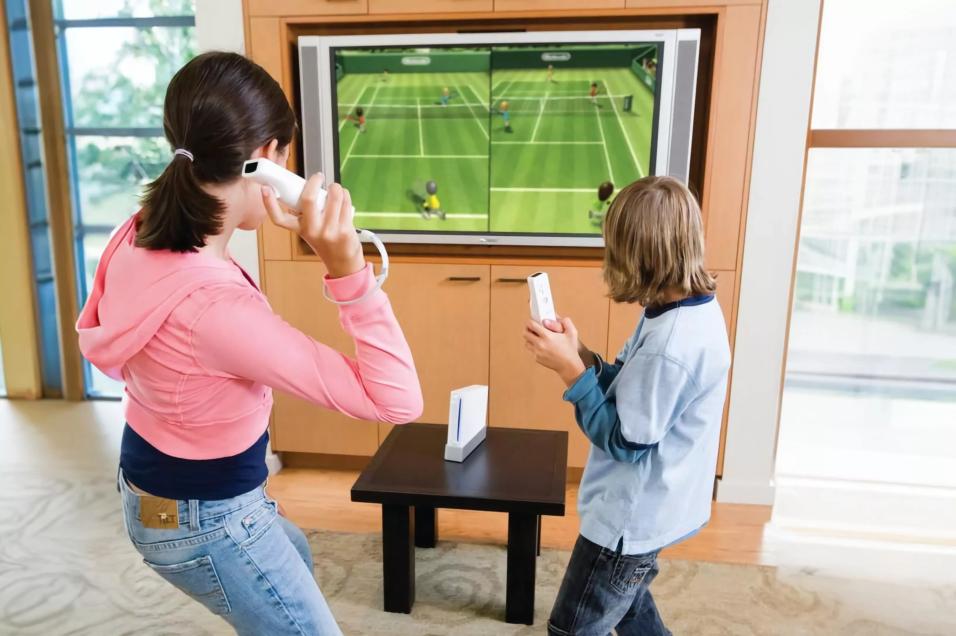 Two children playing a tennis video game with motion controllers in front of a television
